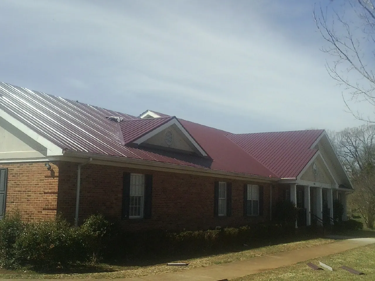 Red metal roof with gabled entries on a long brick building, from a Hail Damage Roof Repair job in West Salem
