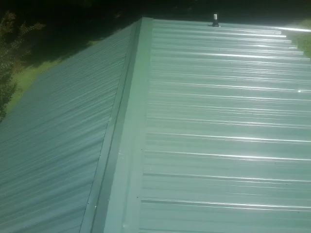 New green metal panels meeting at the ridge of a roof — Flat Roof Repair work by our crew in West Salem