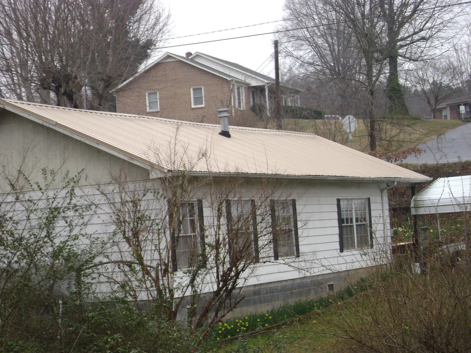 Tan metal roof on a white sided house set into a hillside — Commercial Roofing by Roofing Brothers in West Salem
